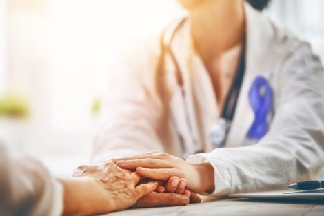 Doctor wearing awareness ribbon holds patients hand