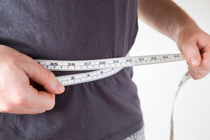 Man measuring waist size with tape measure