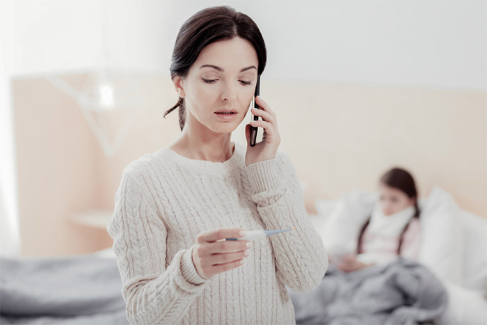 Mother reads thermometer while calling doctor