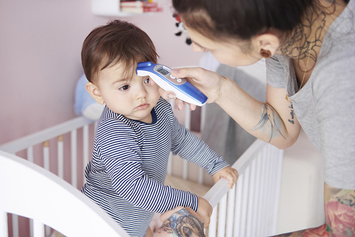 Mother uses forehead thermometer on baby standing in crib