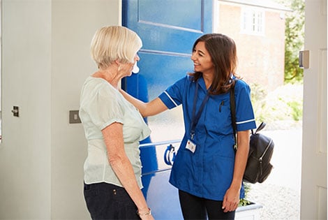 Elderly woman greeting home health nurse wearing nursing bag