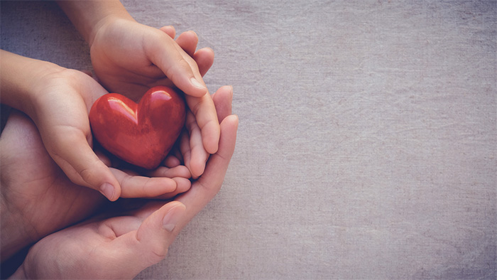 Childs hands inside adult hands holding red heart