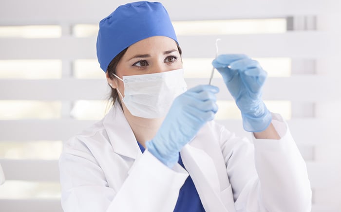 Dentist wearing surgical mask and scrub cap examines curette