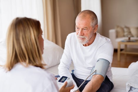 Female doctor checking senior man’s blood pressure at home