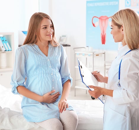 Female doctor with clipboard examining pregnant woman on exam table