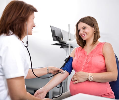 Female nurse checking pregnant woman’s blood pressure