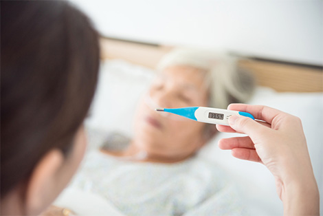 Female nurse checking patient’s temperature on thermometer