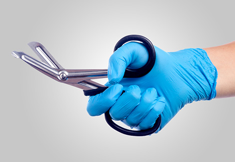 Hand with blue latex gloves holding trauma sheers against a white background