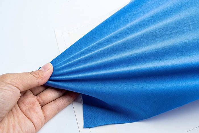Hand pulling on blue fabric to show stretch