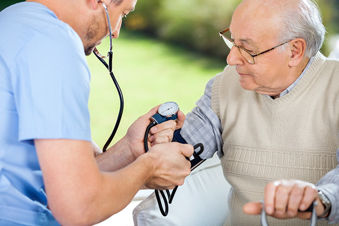 Male home health aide measuring senior patient’s blood pressure