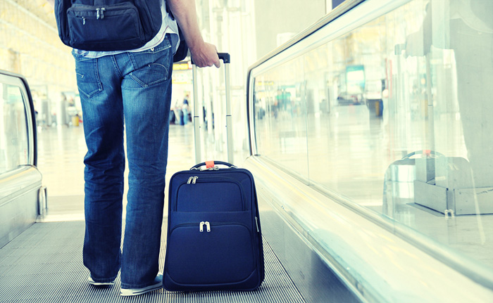 Man pulls rolling suitcase on airport moving sidewalk