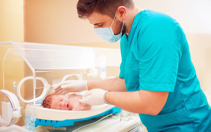 Neonatal intensive care RN examines baby in incubator