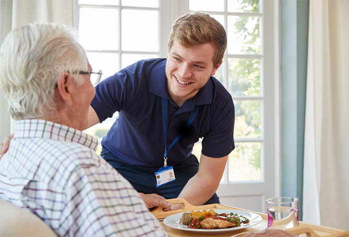 nursing assistant serving dinner to senior patient