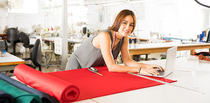 Woman on laptop with fabrics working in a textile factory